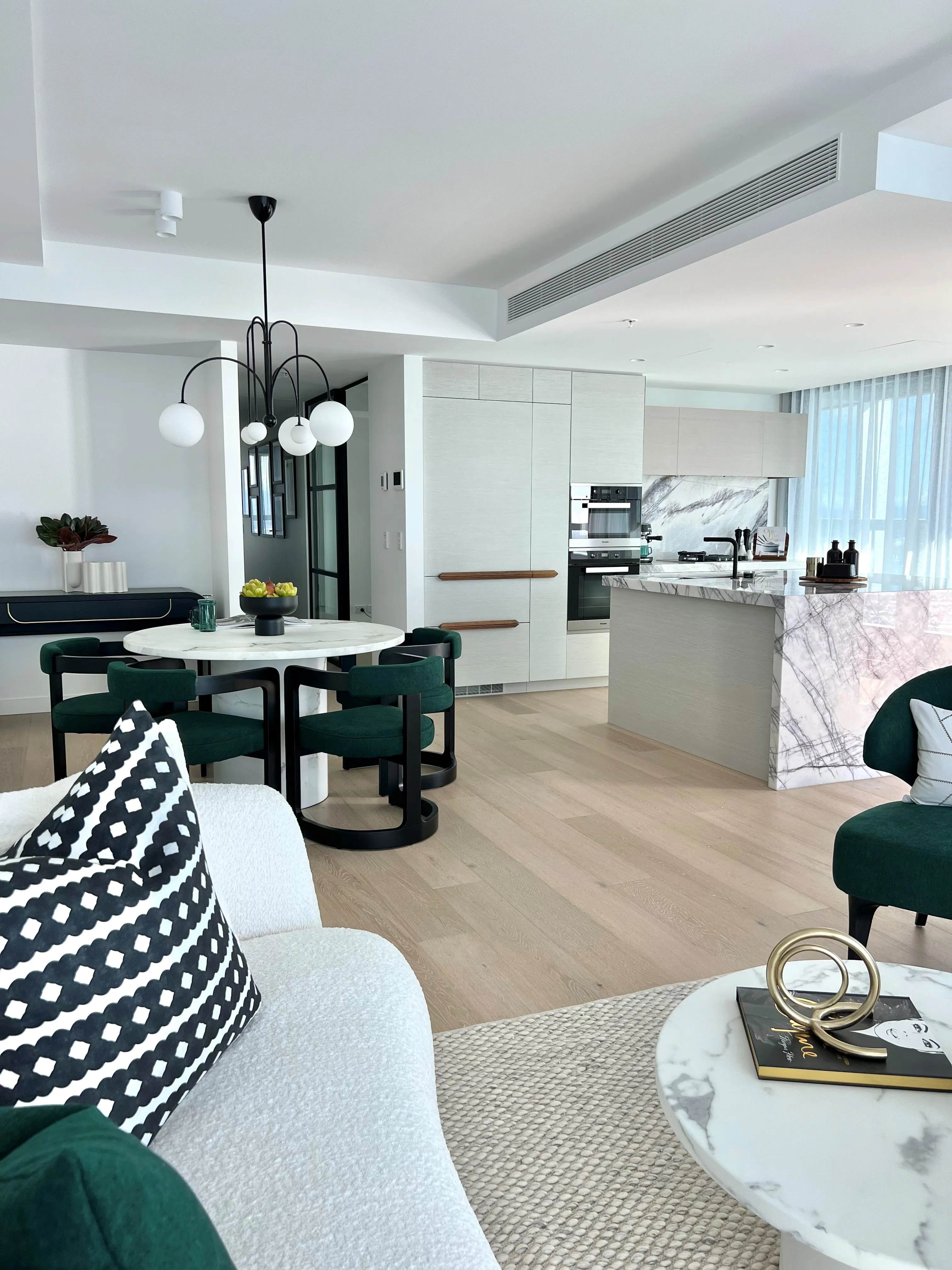 Open-plan apartment with cream bouclé sofa, emerald dining chairs, marble table and globe pendant